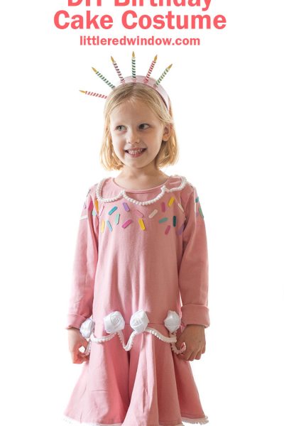 girl in pink birthday cake dress with sprinkles and white frosting rosettes smiling and standing on a table