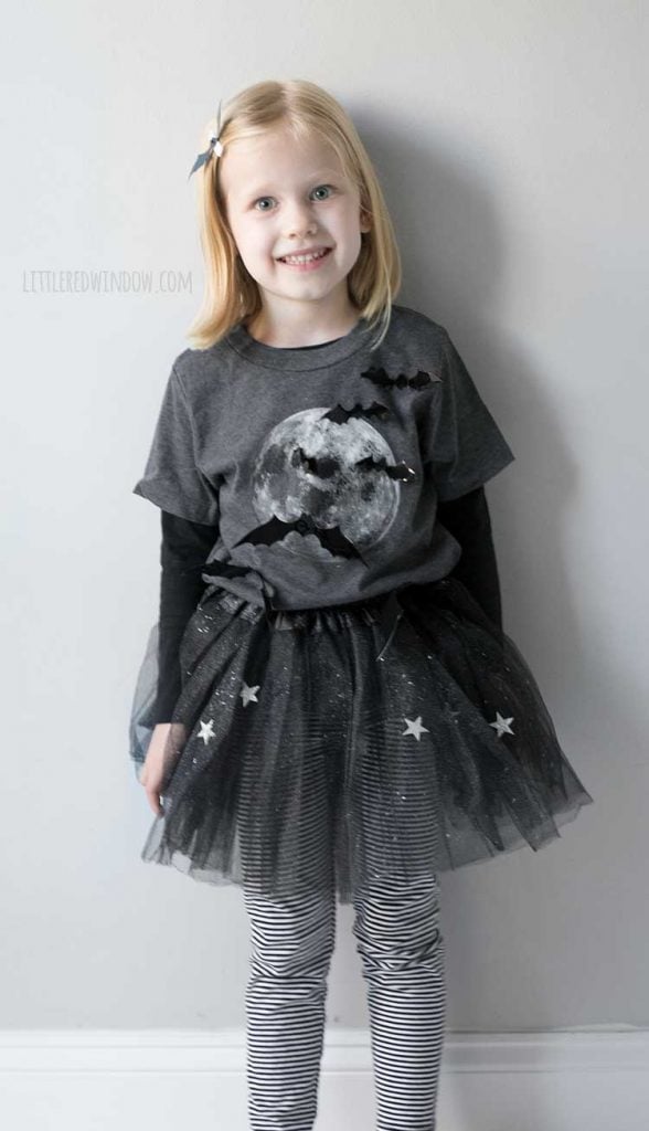 smiling girl wearing bat girl costume with 3D bats over a shirt with a full moon on it and sparking stars tutu
