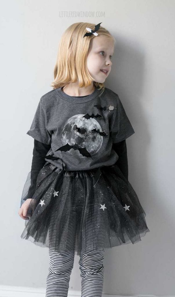 smiling girl looking off to the right wearing bat girl costume with 3D bats over a shirt with a full moon on it and sparking stars tutu