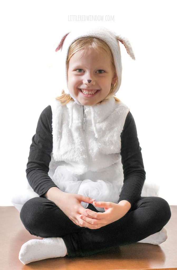 smiling girl sitting with hands in her laps wearing white fluffy easy diy sheep costume