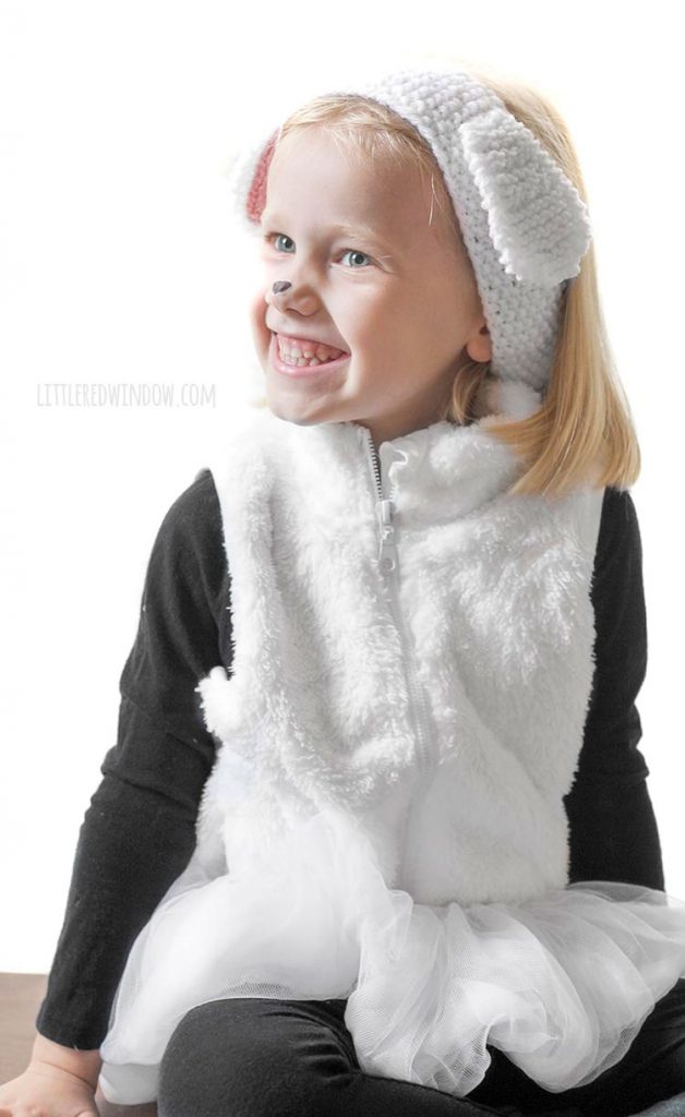smiling girl wearing white furry vest white tutu and white sheep headband and smiling