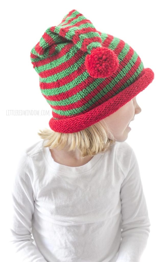 little girl looing off to the right and wearing a red and green striped stocking cap with rolled brim and red pom pom