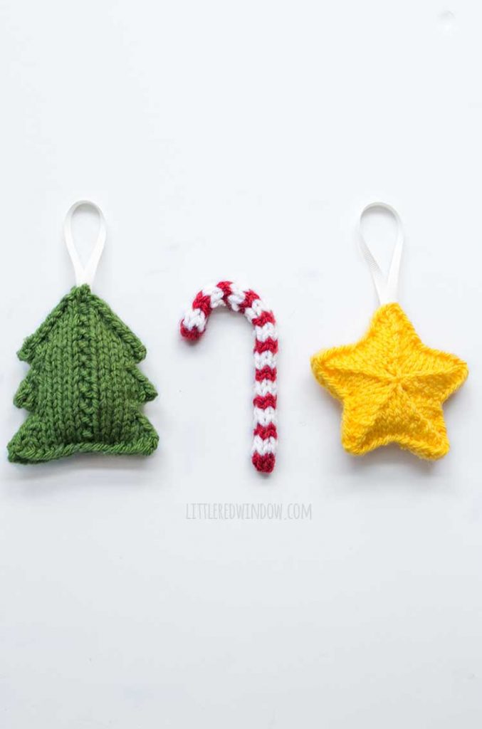 a green tree red and white candy cane and yellow start knit christmas tree ornaments in a row on a white table
