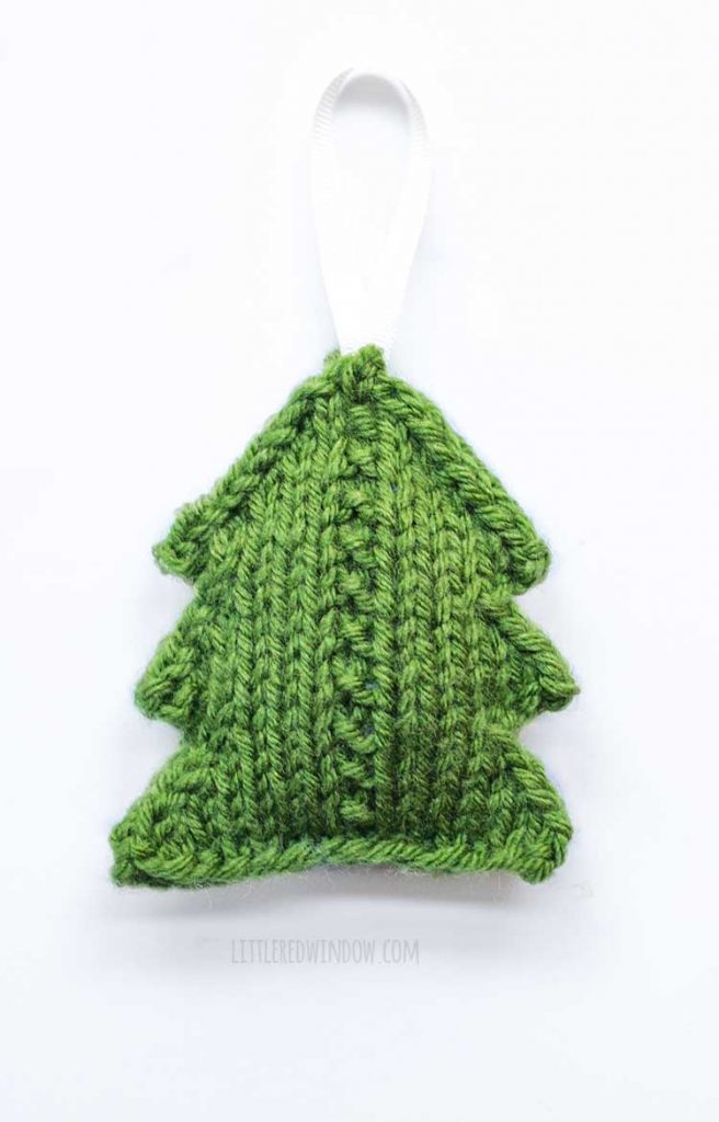 green knit christmas tree shape with a white ribbon hanging loop on top laying flat on a white background