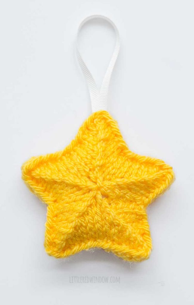 yellow knit star shape with a white ribbon hanging loop on top laying flat on a white background