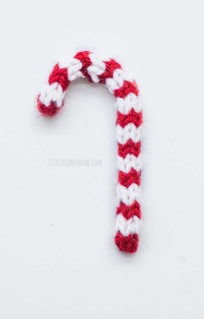 red and white striped knit candy cane shape lying flat on a white background