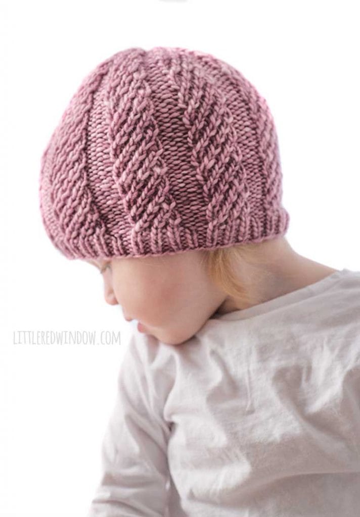 side view of baby wearing mauve knit twisted rib hat and looking down over her right shoulder