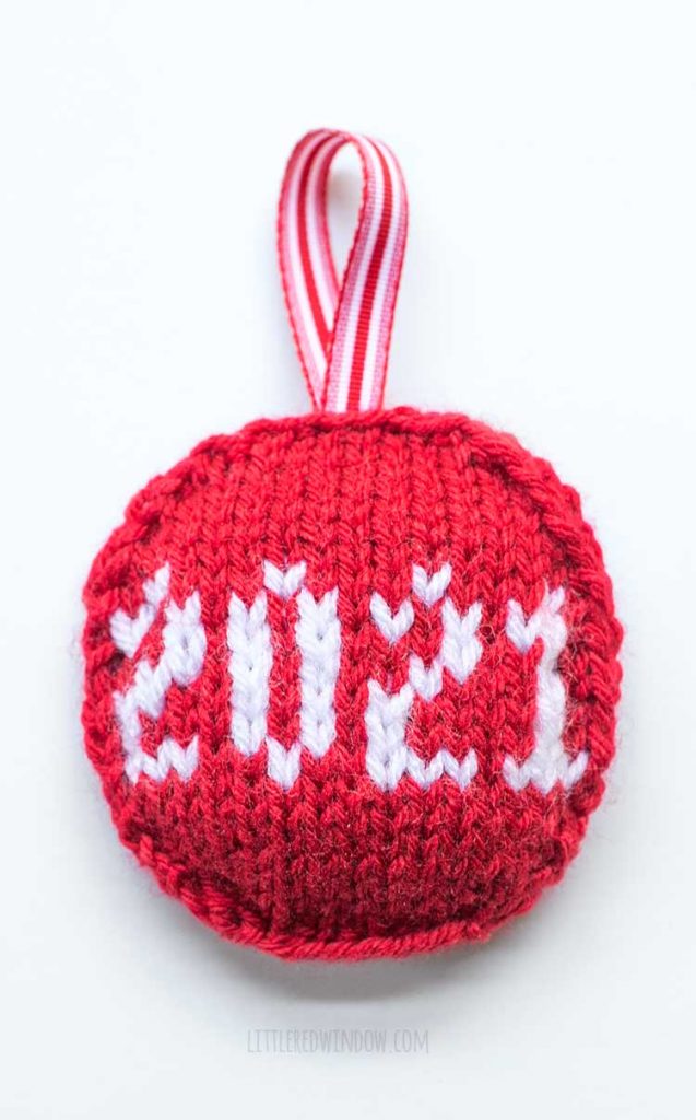 red flat circular knit ornament with red ribbon hanging loop with the date 2021 knit on the front in white yarn