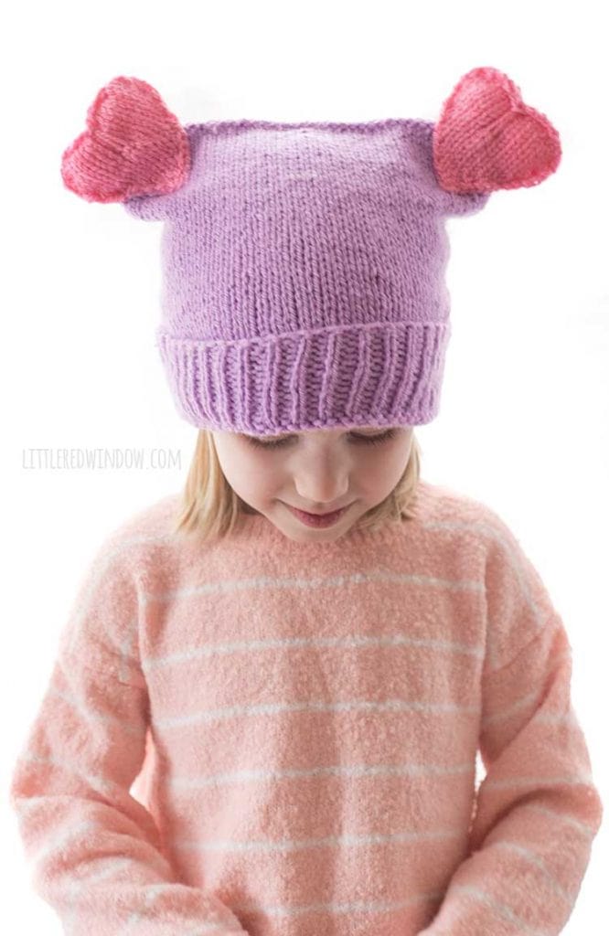closeup of purple knit hat with two pink hearts on top
