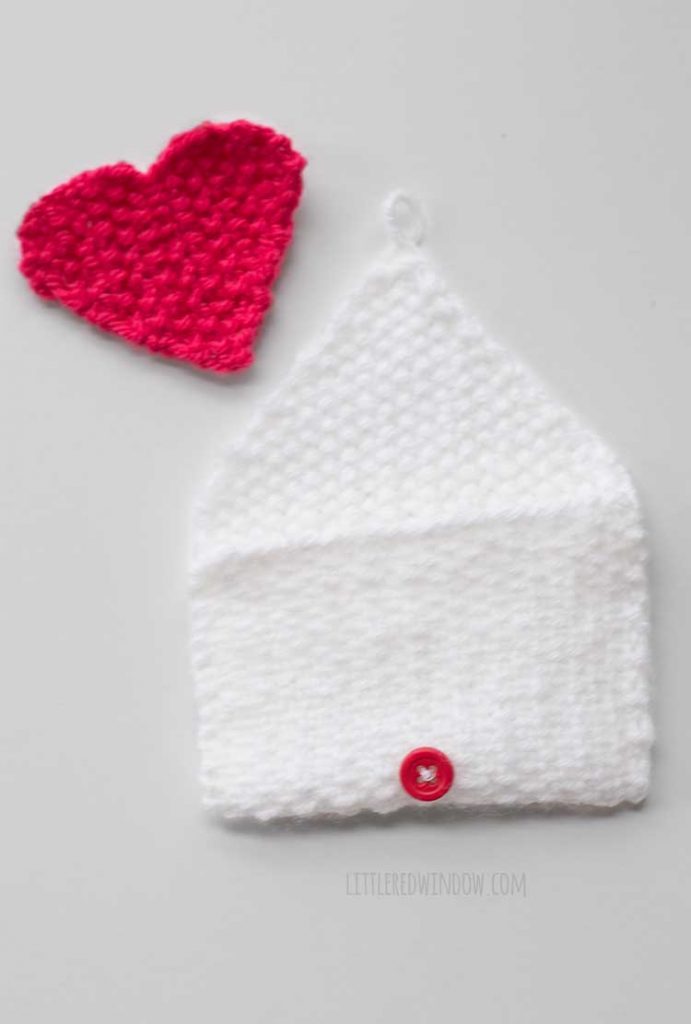 open white knit envelope shape with red knit hear just abbove it on a light gray background