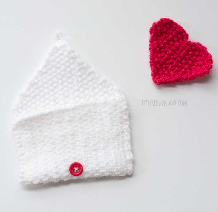 finished envelope shape with red button sewn on and red knit heart shape next to it