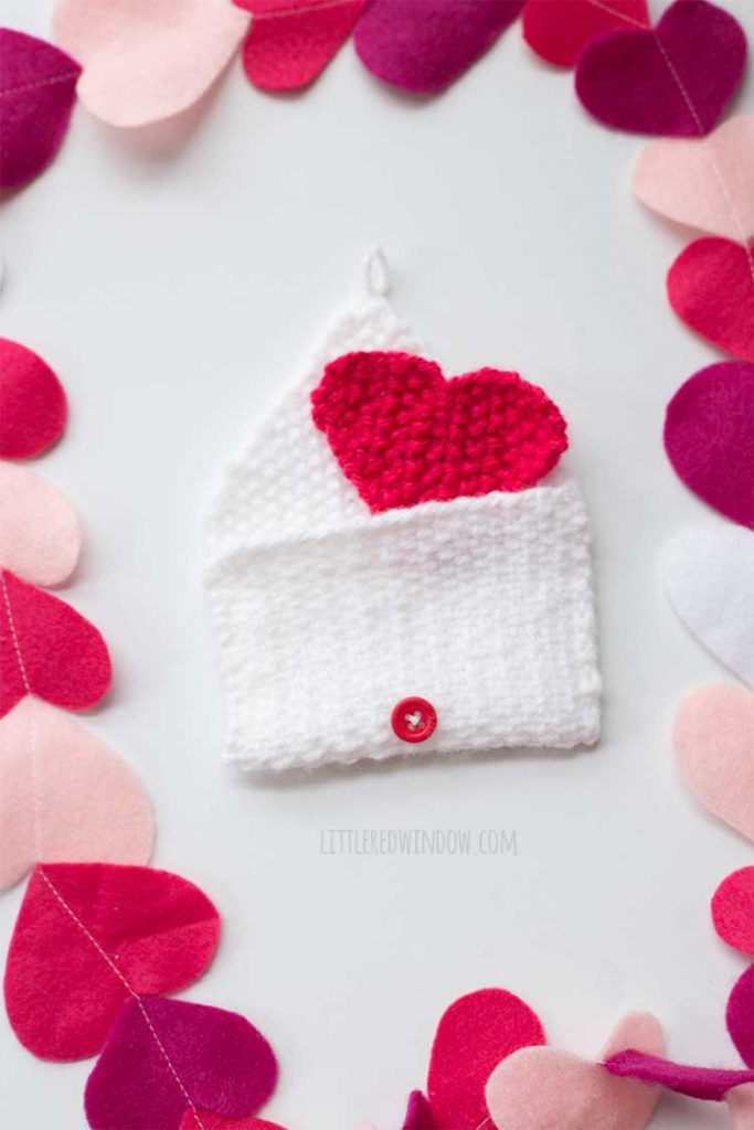knit heart and envelope on a white background with multicolored pink and red felt hears lined up around the edges of the image