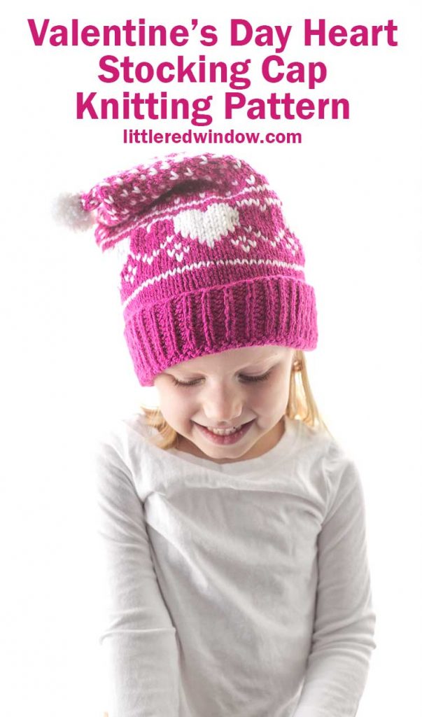 little girl in white shirt wearing magenta colored knit stocking cap with white hearts and white dots on it