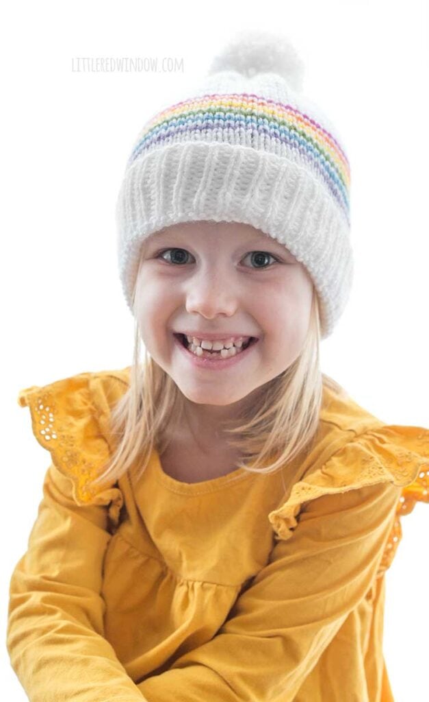 smiling girl wearing white knit classic rainbow stripe hat