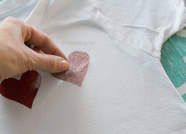 hand peeling protective film off pink glitter heart shape on white tshirt