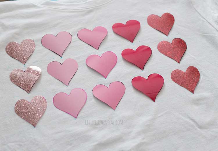 18 iron vinyl heart shapes in shades of pink arranged on a white shirt
