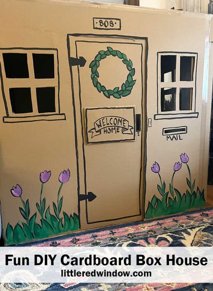 large toy house made out of  a cardboard box with a door two windows and flowers painted on the front