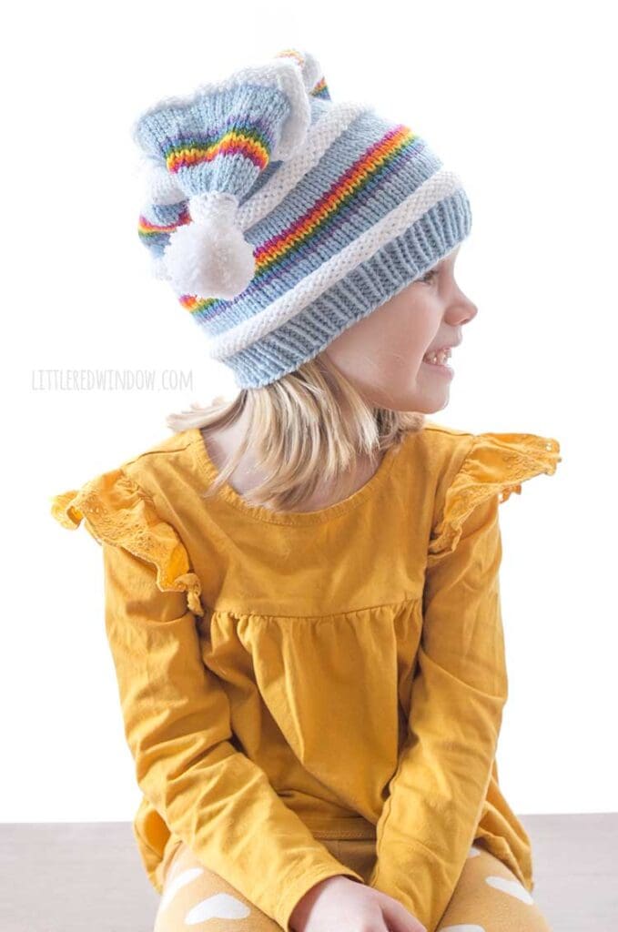 girl in yellow shirt wearing knit stocking cap with rainbow blue and white stripes looking off to the right