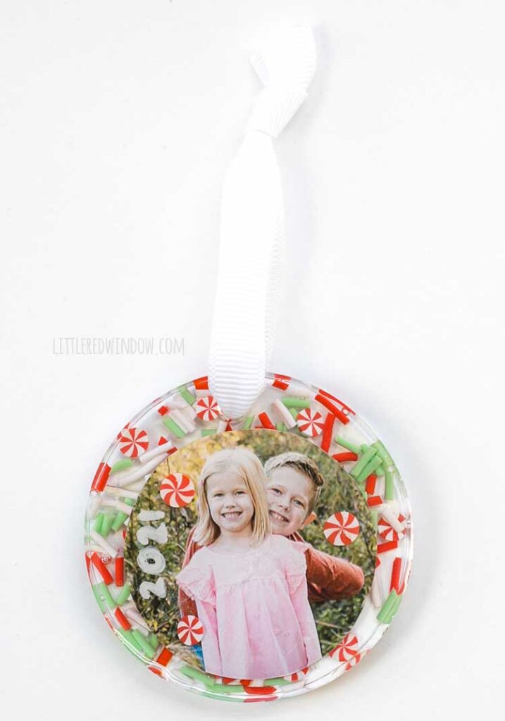 one finished sprinkle resin christmas ornament with a white ribbon loop tied at the top on a white background