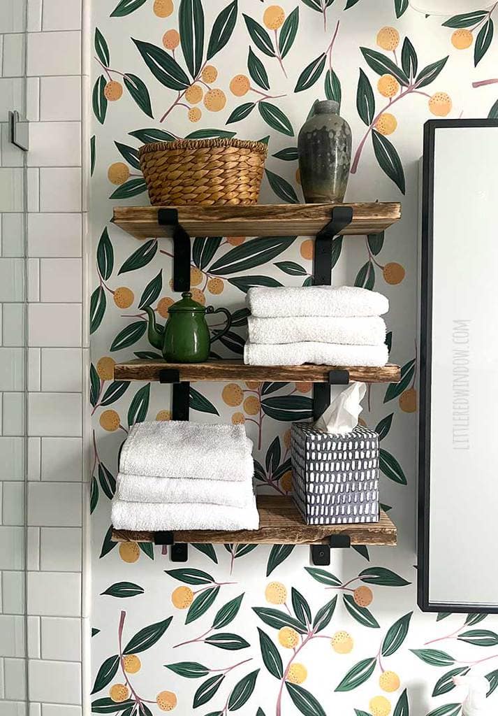 closeup of tangerine wall decals as wallpaper behind three wooden shelves that hold towels tissue and baskets