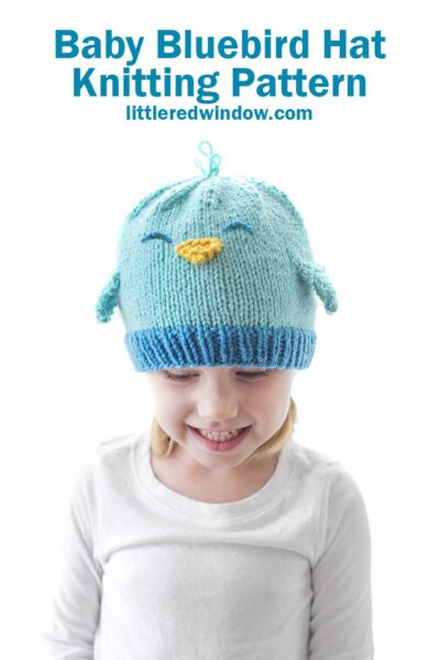 little girl in white shirt wearing a knit hat that looks like a bluebird