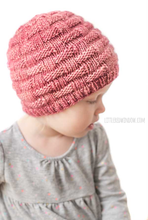 little girl wearing red knti hat with knit and purl basketweave texture looking back over her left shoulder