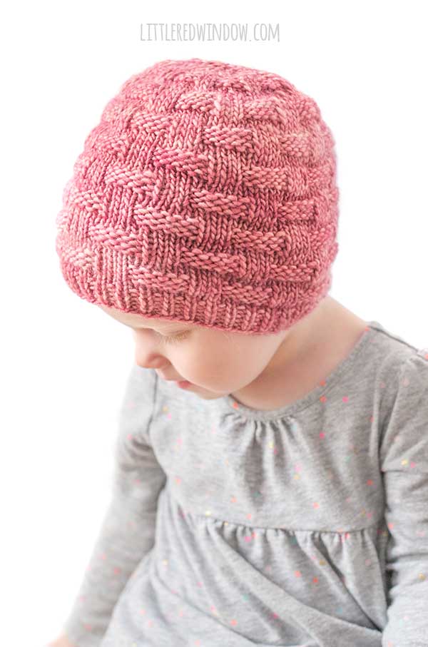 little girl wearing red knit hat with knit and purl basketweave texture looking back down to the left