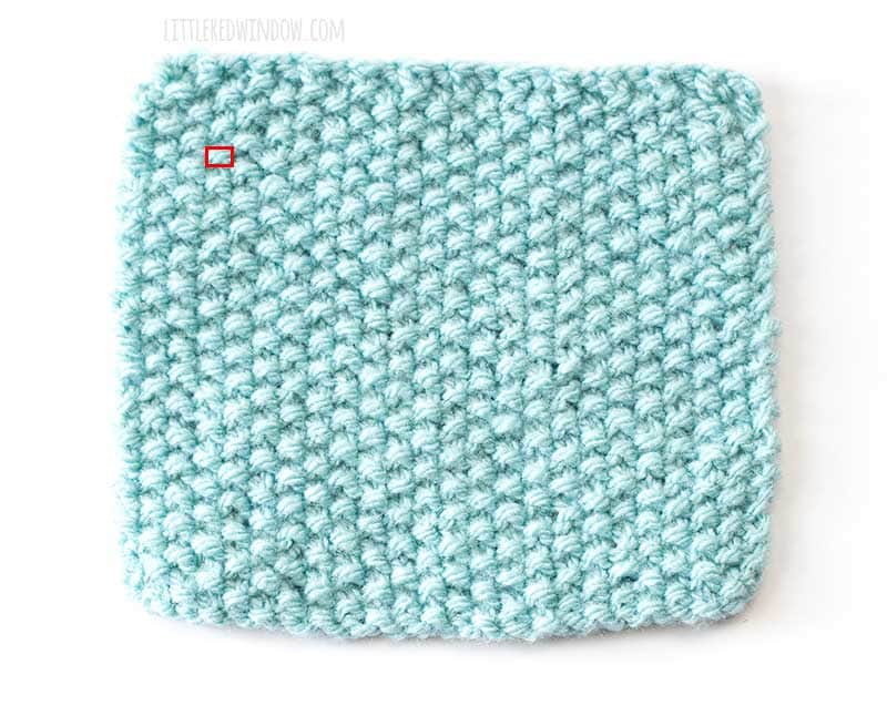a light blue swatch of seed stitch knitting with a single purl stitch outlined in red