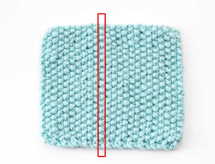 a square of light blue seed stitch knitting with a single column of stitches outlined in a red rectangle