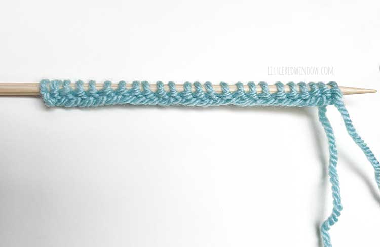 a knitting needle with light blue yarn showing the wrong side of the long tail cast on method