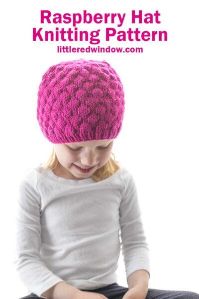 little girl in white shirt and knit hat that looks like a raspberry