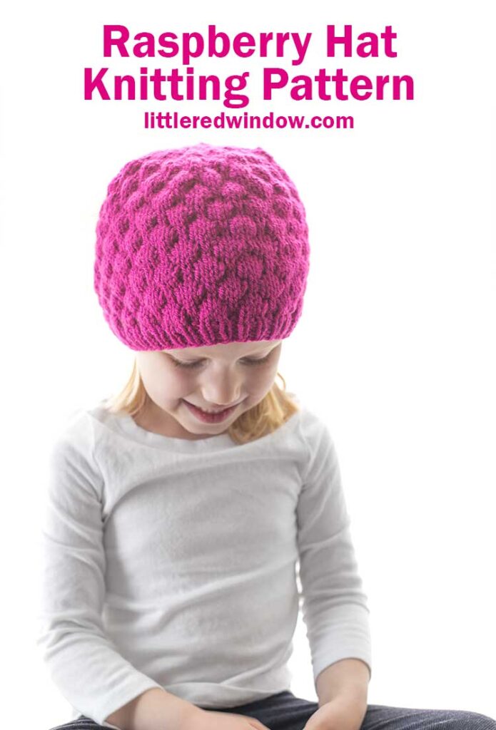 little girl in white shirt and knit hat that looks like a raspberry