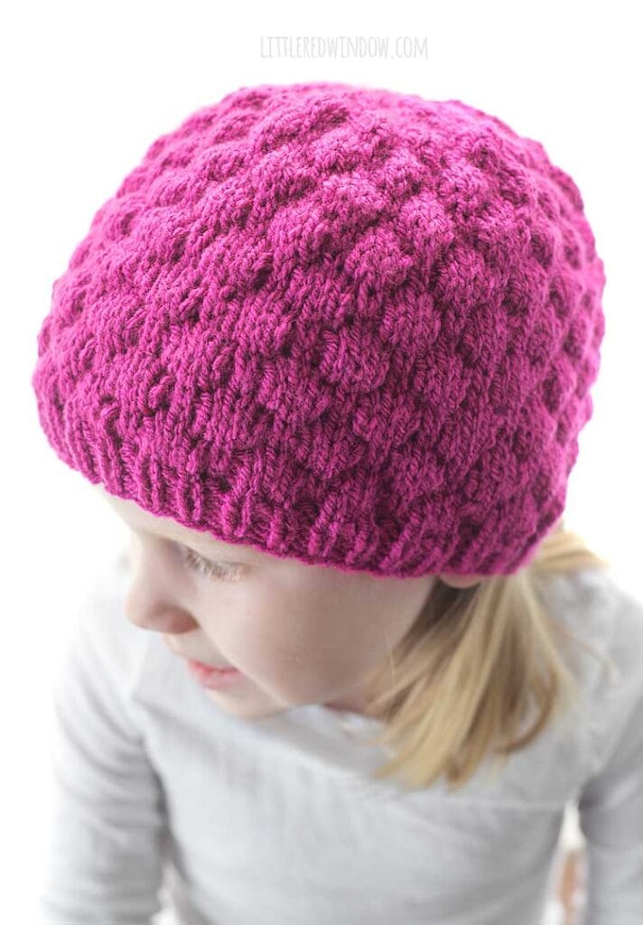 closeup of bubble knitting stitch on raspberry hat knitting pattern on girl looking off to the right