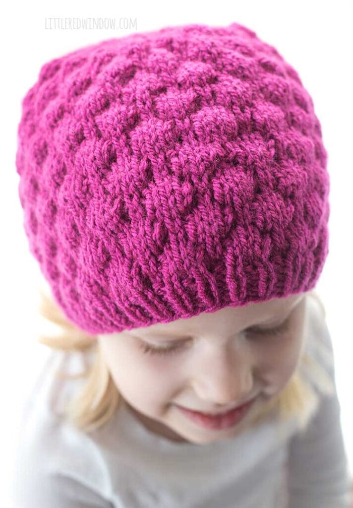 closeup of bubble knitting stitch on raspberry hat knitting pattern on girl looking down