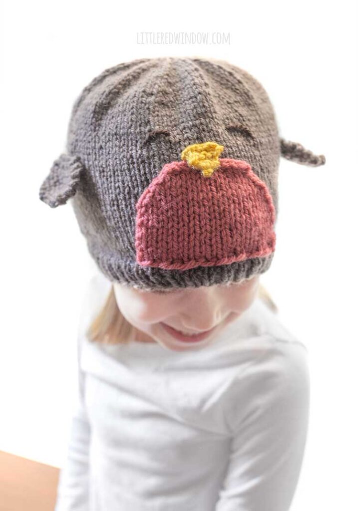 little girl wearing robin hat with wings looking down