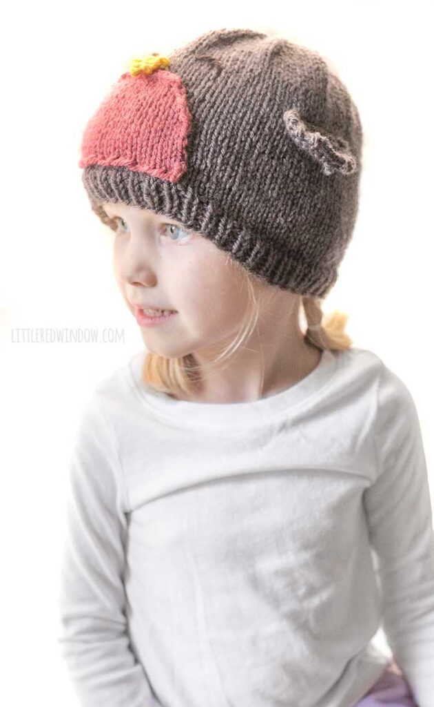 little girl wearing brown knit hat that looks like a bird looking off to the left