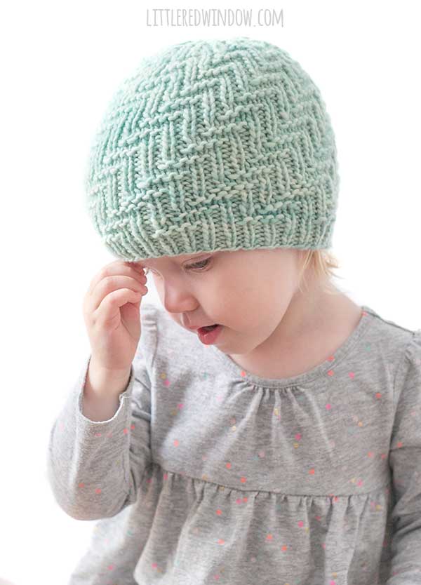little girl touching the brim of her mint green woven zig zag knit hat