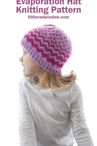 little girl in white shirt looking off to the left and wearing lavender knit hat with decreasing width zig zags in raspberry