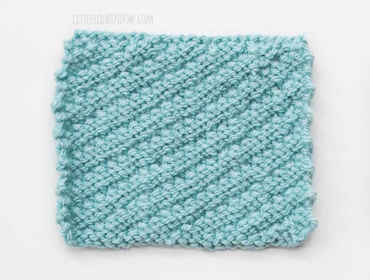 the wrong side of a light blue rectangle of diagonal stitch knitting on a white background
