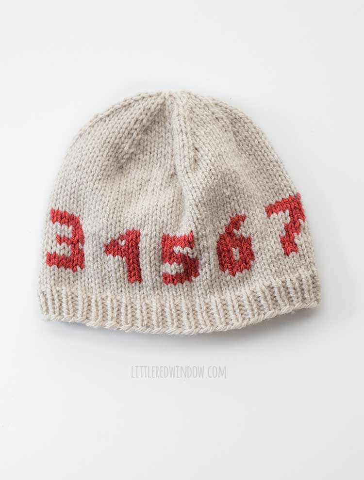 tan knit hat with the number 3 through 7 knit in red around the middle on a white background