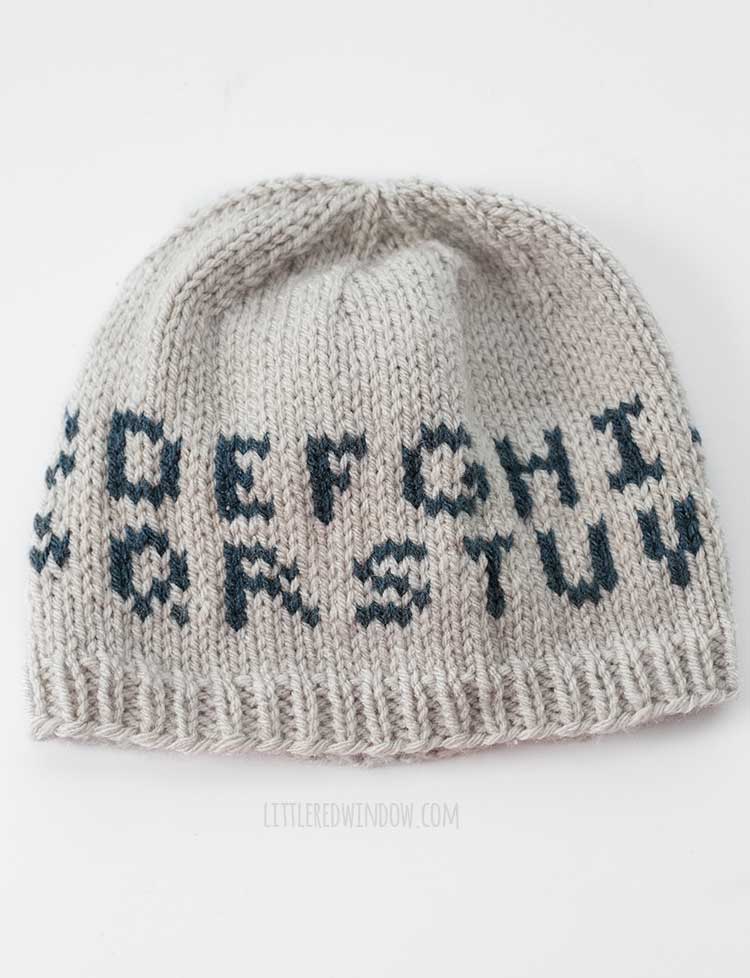 tan knit hat with two rows of letters in dark blue on a white background