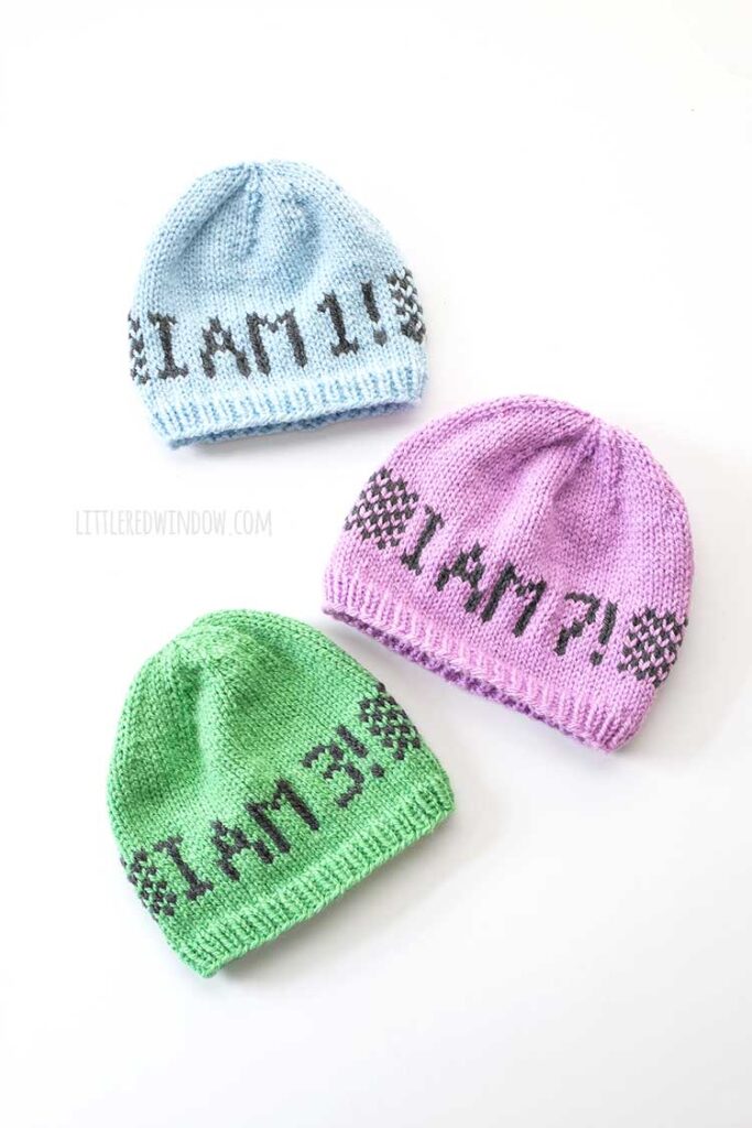 3 knit birthday hats on a white background knit in light blue light green and lavender