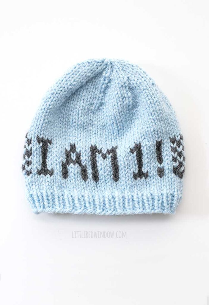 white background with light blue knit baby hat with the words I am 1 on the front in charcoal