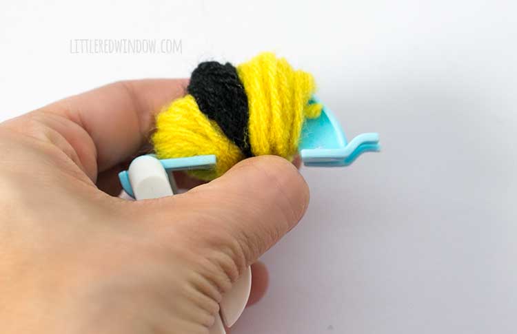 hand holding pom pom maker wound with two yellow and one black stripes