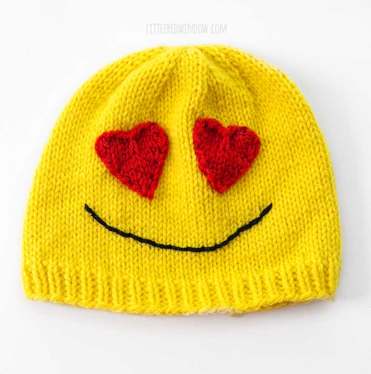 yellow knit hat with red heart eyes and black smile on a white background