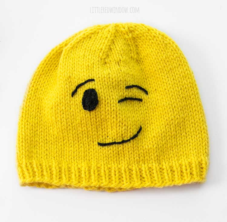 yellow knit winking emoji hat on a white background