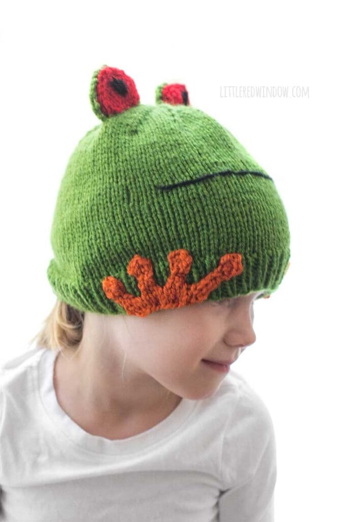 little girl wearing a white shirt and colorful tree frog hat and looking off to the right