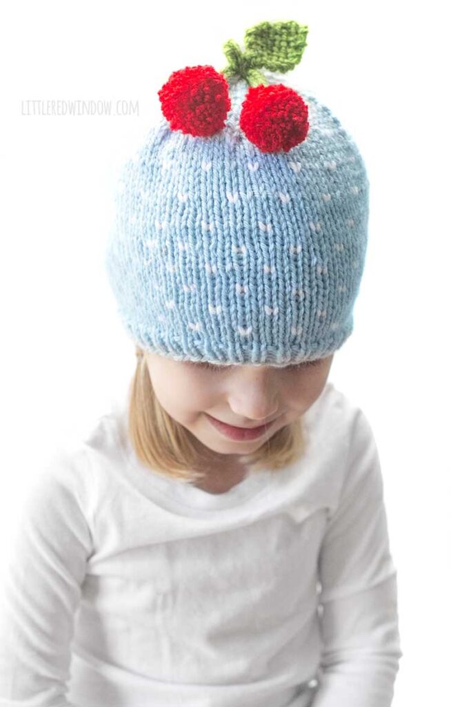 little girl in light blue knit hat with two red cherries on top