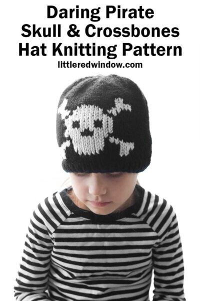 child in black and white striped shirt wearing a black knit hat with a white skull and cross bones knit on the front and looking down at their lap