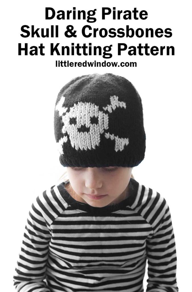 child in black and white striped shirt wearing a black knit hat with a white skull and cross bones knit on the front and looking down at their lap